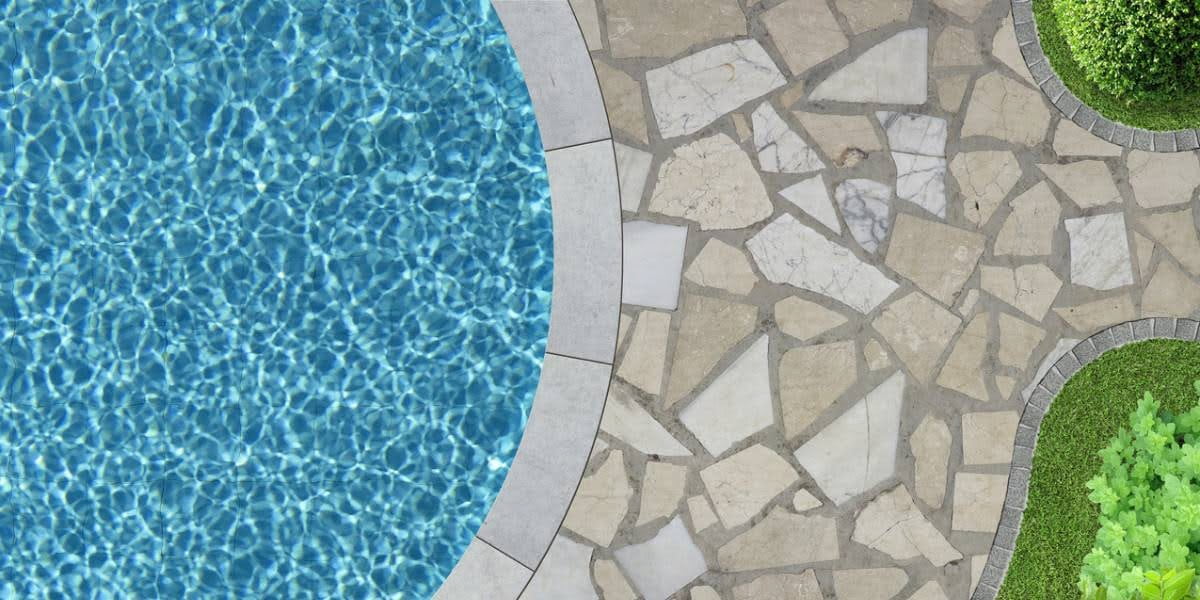 pool-deck-design-trends (2) Overhead view of a swimming pool and stone patio showcasing modern pool deck design trends with natural pavers and clean landscaping.