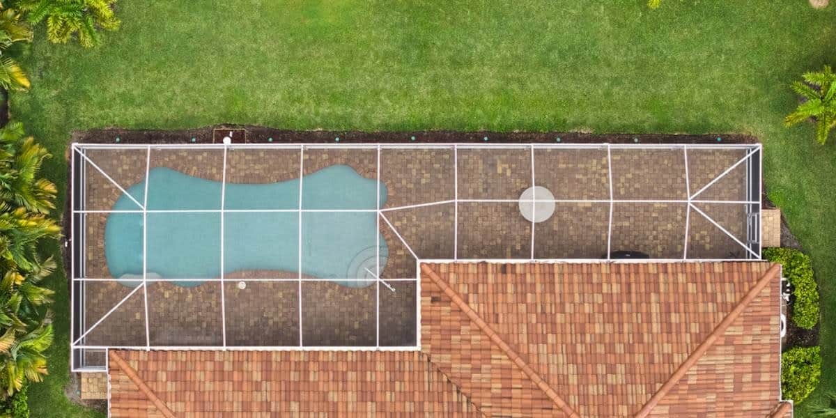 pool-paver-ideas (1) Aerial view of a backyard pool patio with screened enclosure showcasing pool paver ideas using brick pavers for a clean and organized layout