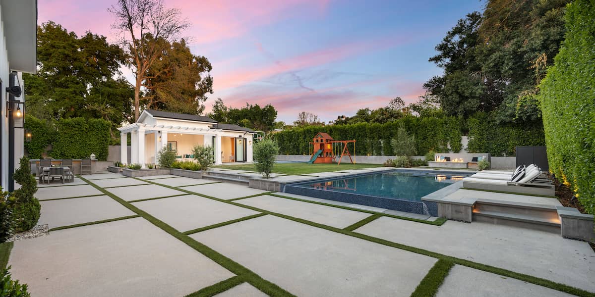 Modern backyard with pool, lounge area, and children's playset showcasing popular pool deck paver colors for style and comfort