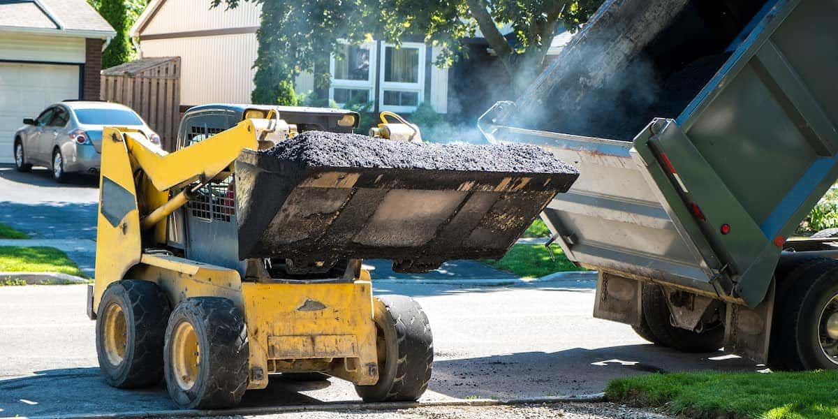 Construction equipment loading asphalt for driveway installation in a residential neighborhood, illustrating how long does a paved driveway last.