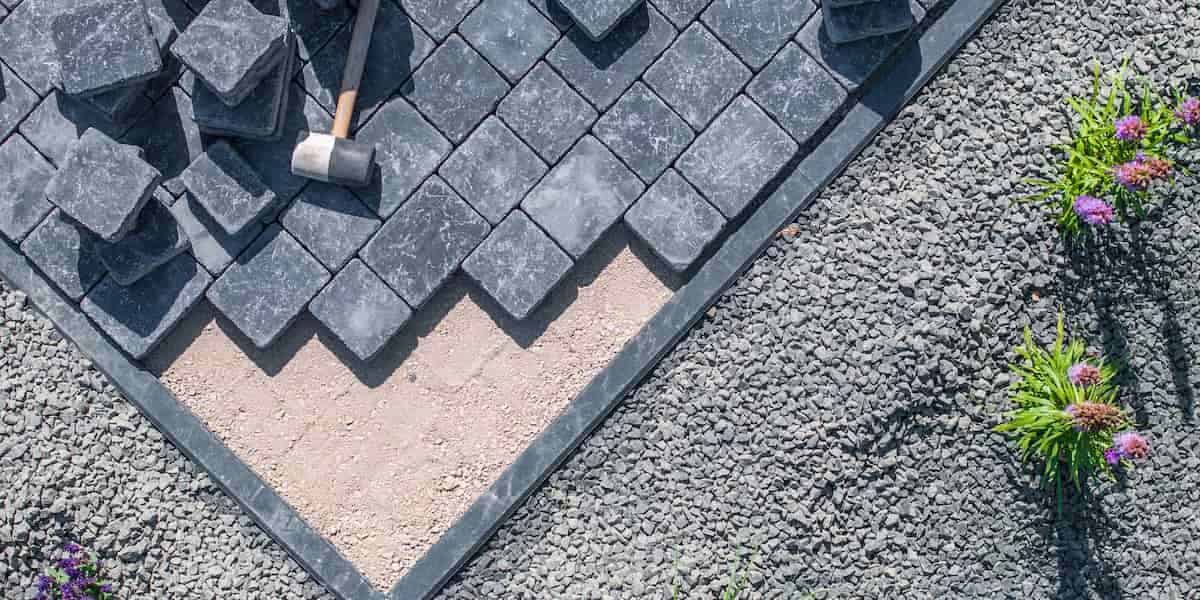 Close-up of pavers being installed on gravel base with a rubber mallet, representing pavers vs concrete driveway design and durability comparison.