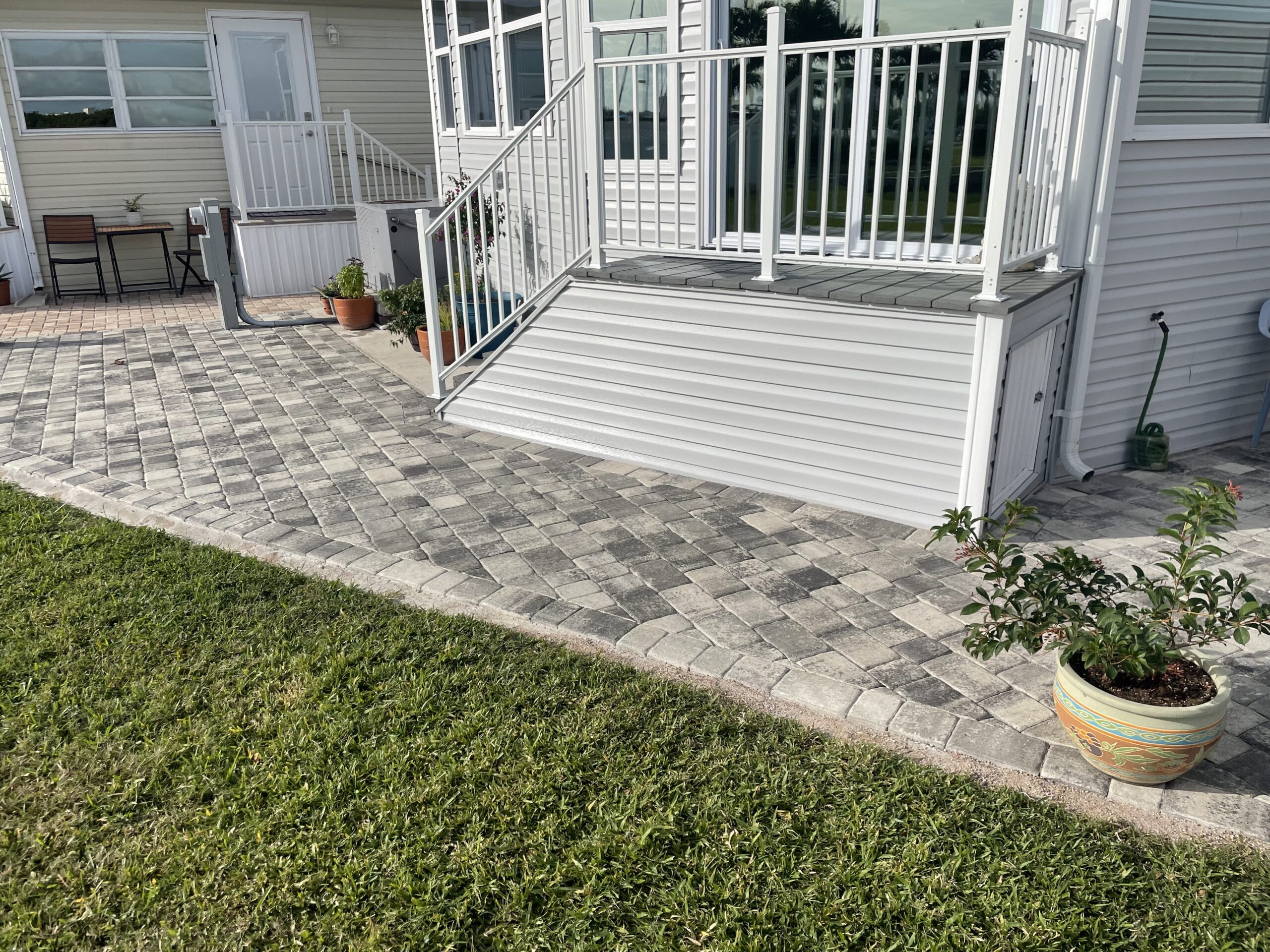 Curved paver patio and walkway installation beside residential home with steps and railing
