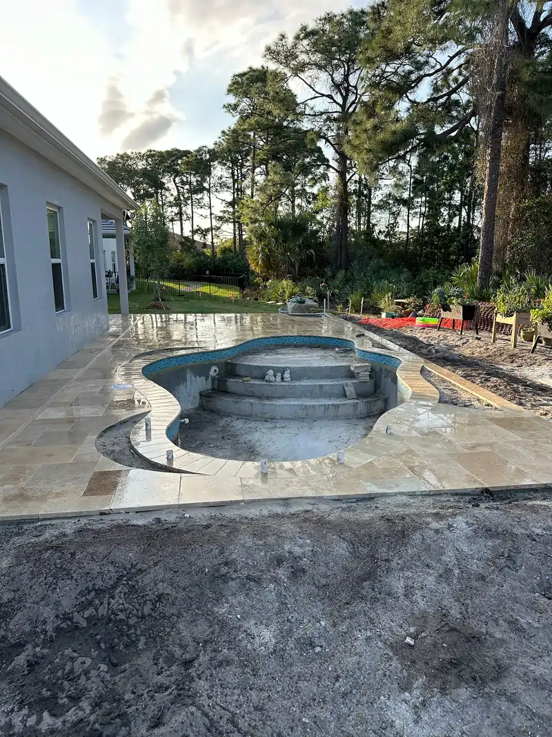 Pool paving installation project with stone pavers surrounding custom backyard pool in St Lucie County